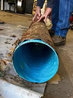 Hands holding a cutaway of a blue liner inside a short section of host pipe.